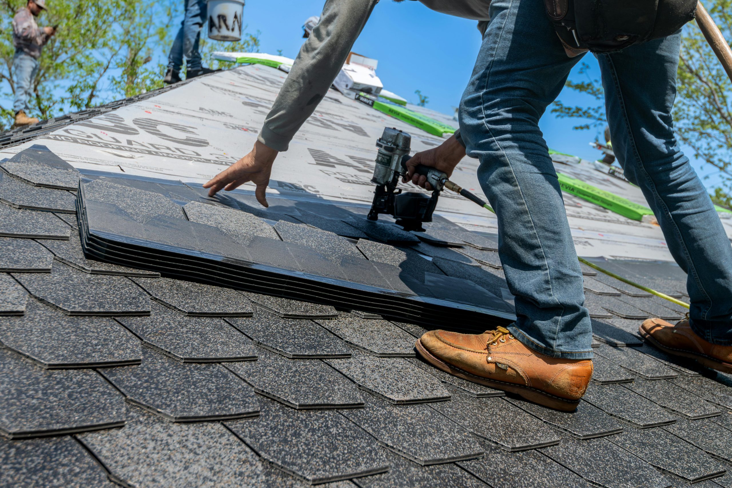 Services Roofer using nail gun for shingle installation on residential roof.